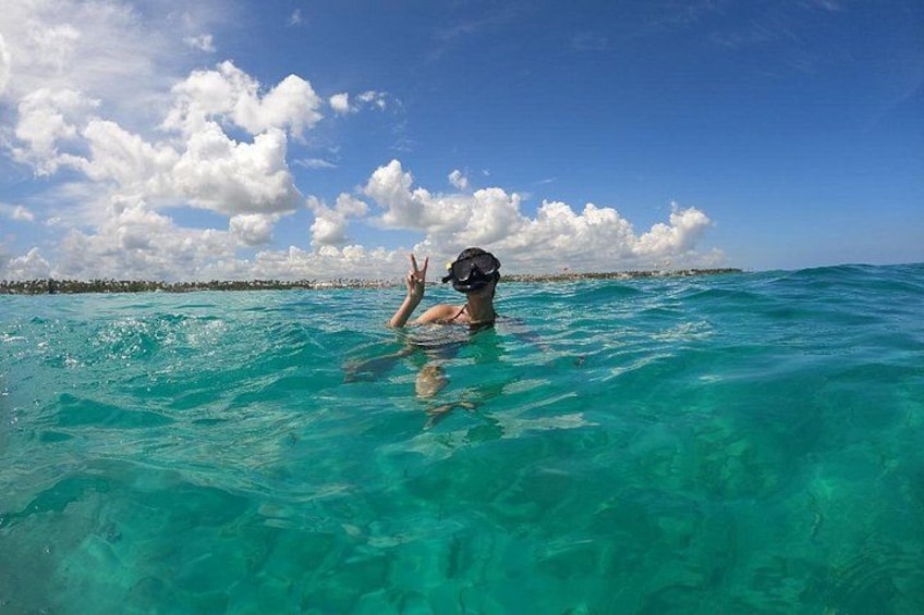 A person snorkeling in clear turquoise water with a distant shoreline and a partly cloudy sky. 2