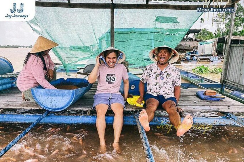 Tres personas sentadas en una plataforma flotante con una red en la parte superior, rodeadas de agua y barcos. 3