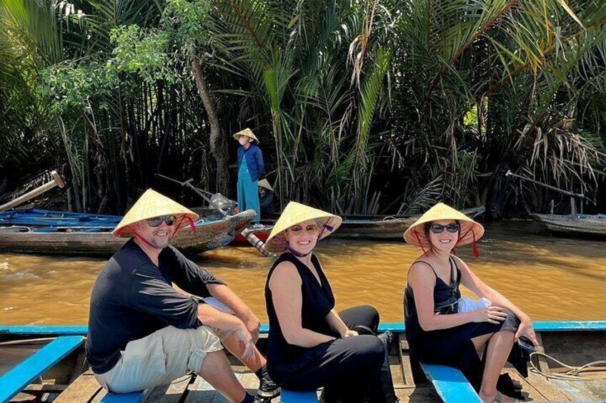 Three people in a boat wearing conical hats, surrounded by dense mangrove trees. 5