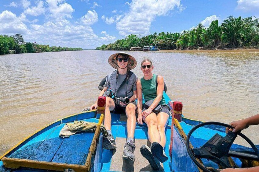 Two people on a blue boat with a river and palm trees in the background. 4