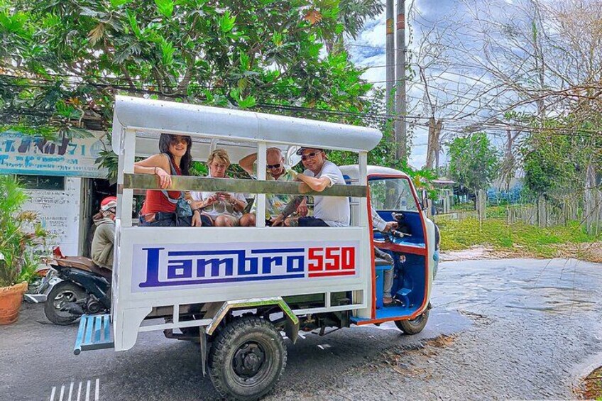 A white and blue truck with the text 'Ambro 550' on its side, parked on a road with trees and a building in the background. 3