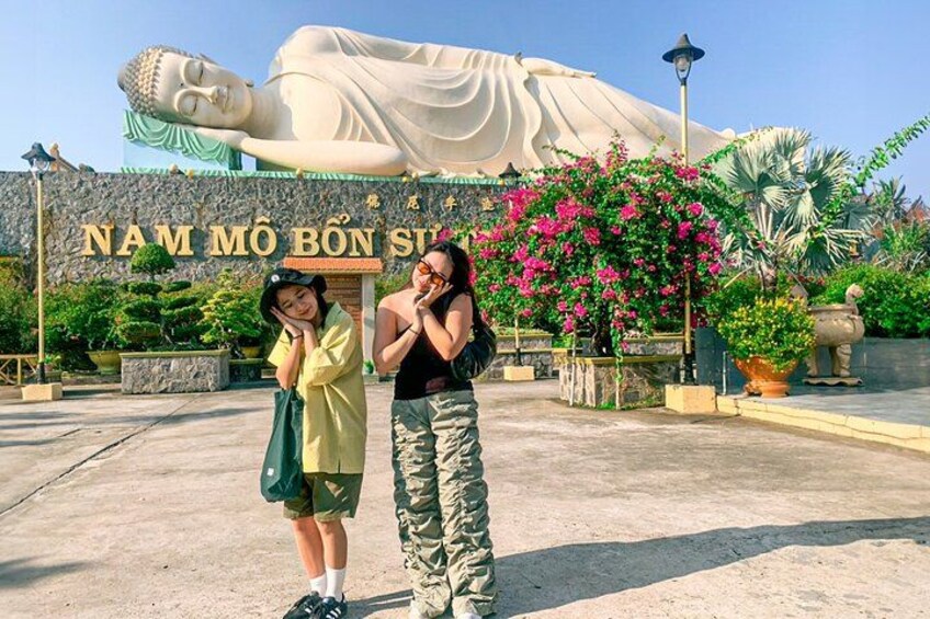 A large Buddha statue, a sign with Vietnamese text, and people posing in front of it. 4