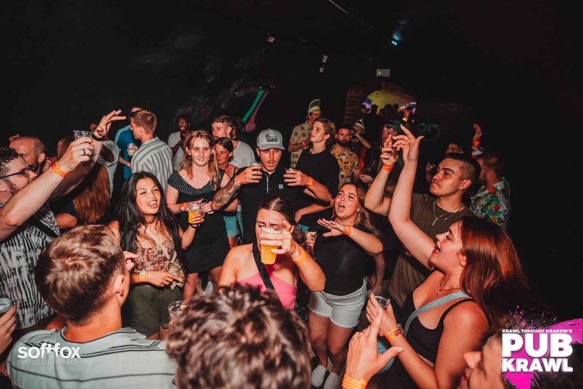 A crowded indoor event with people holding drinks and raising their hands. 5