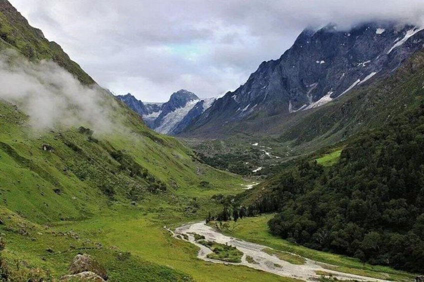 A valley with a river, green hills, and mountains in the background. 2