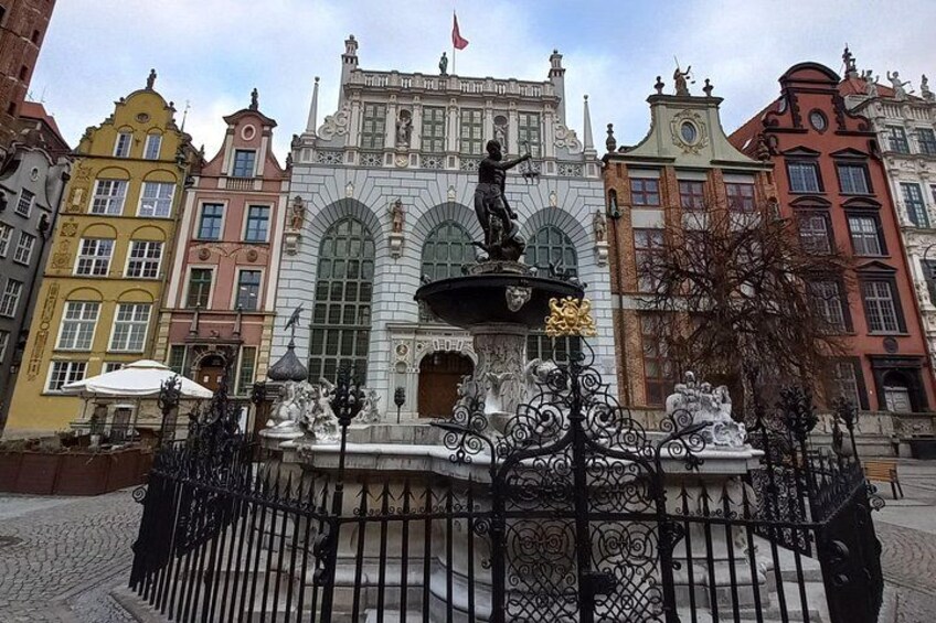 En historisk byggnad med utsmyckad arkitektur, en staty på en fontän och en kullerstensgata. 4