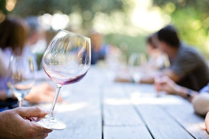 A person holding a wine glass at a wooden table with others seated around it. 3
