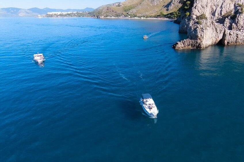 A boat sailing on a clear blue sea with rocky cliffs in the background. 4