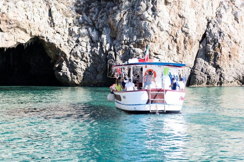 A boat with passengers, a rocky cliff, and clear blue water. 2