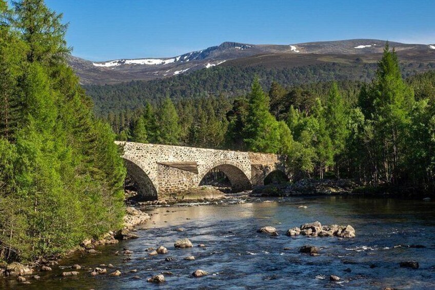 Un puente de piedra sobre un río, rodeado de árboles y montañas. 5