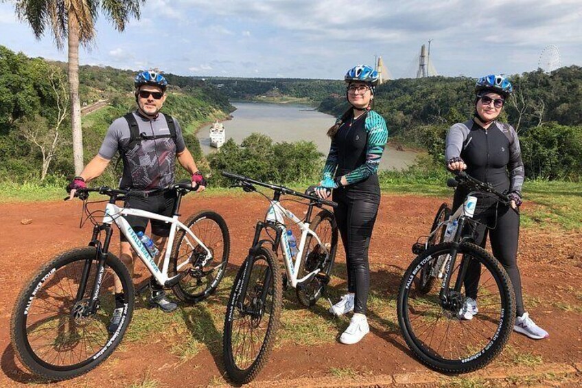 Three cyclists on a dirt path with a river and hills in the background. 5