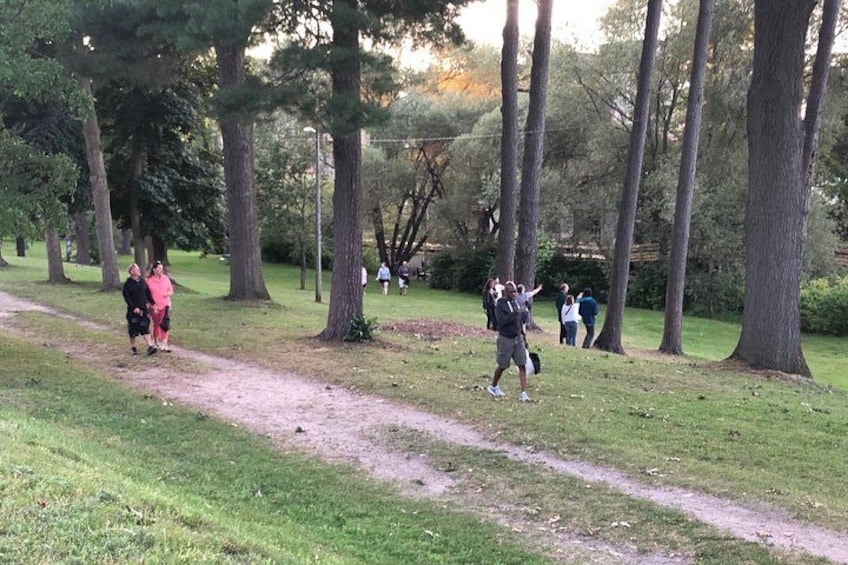 A park with a dirt path, trees, and people walking. 4