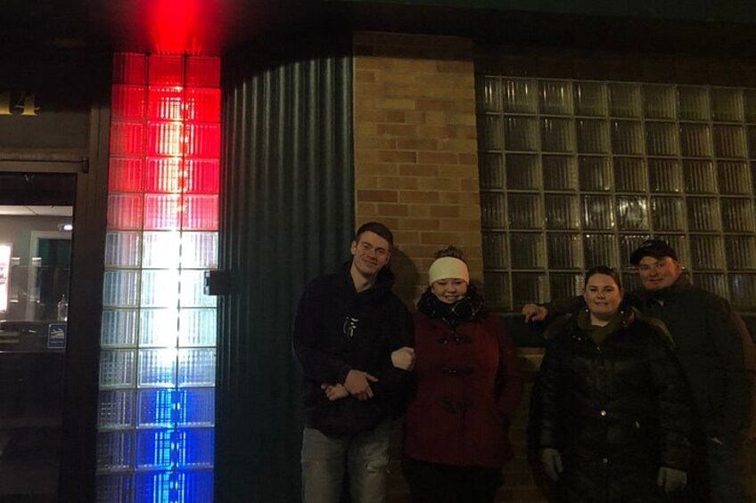 A group of people standing in front of a building with a red and blue illuminated window. 3