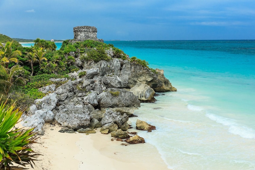 A coastal landscape with a rocky outcrop, a small stone structure, and turquoise waters. 1
