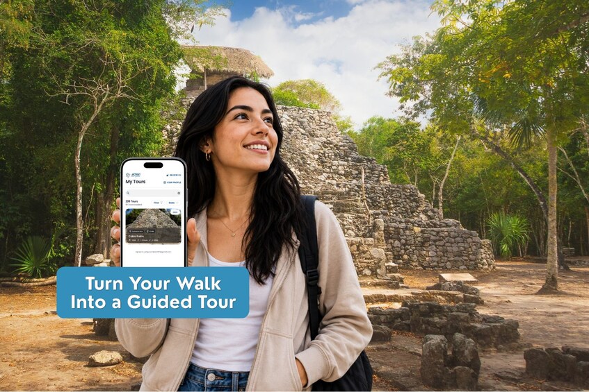 A person holding a smartphone with a travel app interface, standing in front of ancient stone ruins surrounded by trees. 3