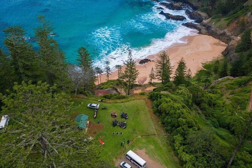 A coastal landscape with a beach, dense forest, and a small group of people gathered near a vehicle. 5