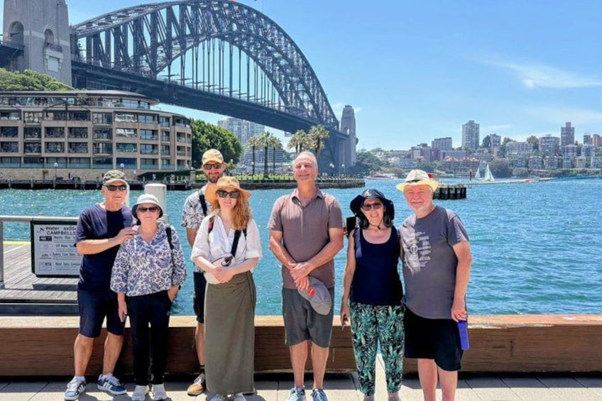 A group of people standing in front of the Sydney Opera House with the Sydney Harbour Bridge in the background. 1