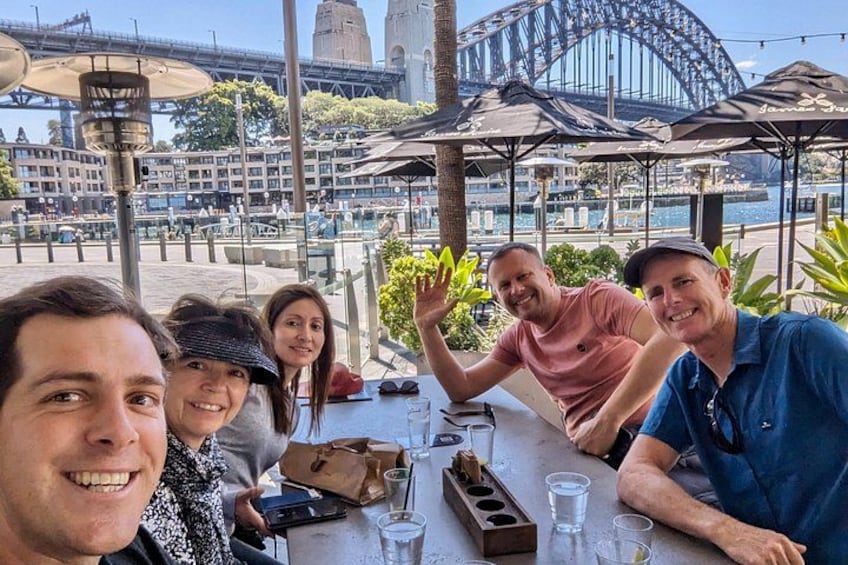A group of people sitting at a table with drinks, a scenic view of a bridge and a tower in the background. 3