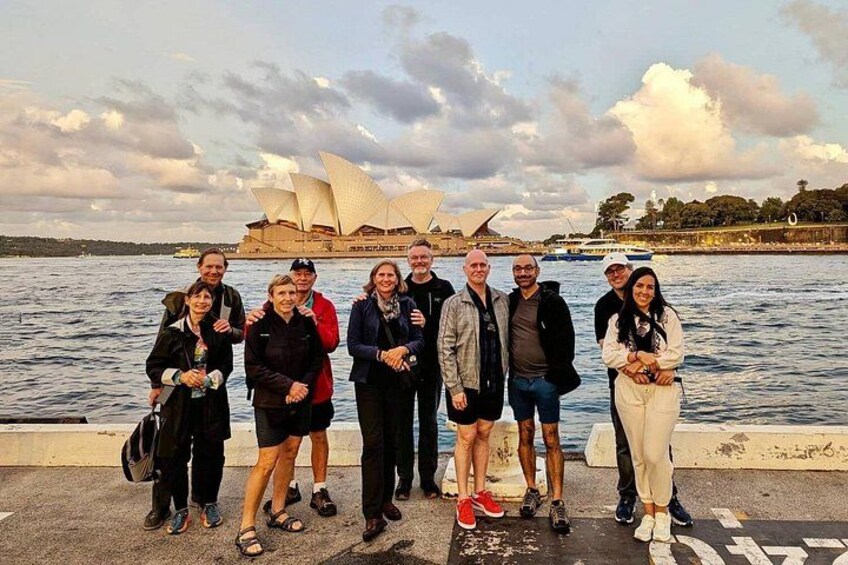 A group of people standing by a waterfront with a large opera house in the background. 5