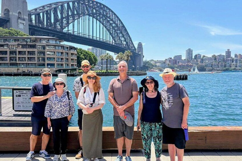 En gruppe mennesker står foran Operahuset i Sydney, med Sydney Harbour Bridge i baggrunden. 1