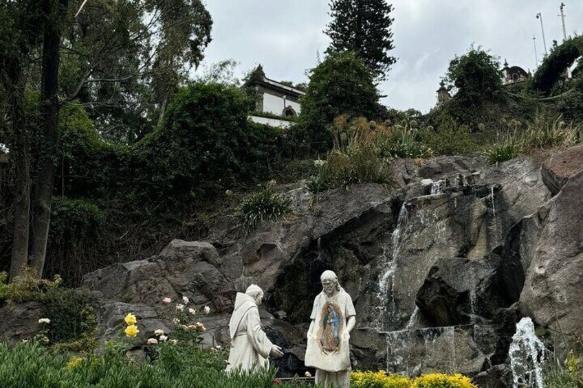 Two statues in a garden with a waterfall and a building in the background. 3