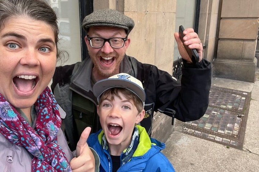 Trois personnes se tiennent devant un bâtiment dont la façade est en pierre et qui est doté d’une grille métallique. 3