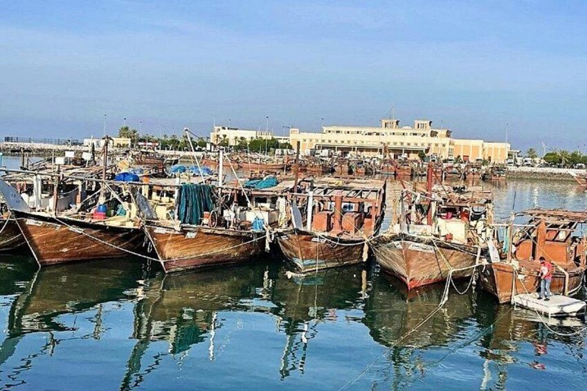 A harbor with several wooden boats docked, a large building in the background, and calm water reflecting the boats. 4