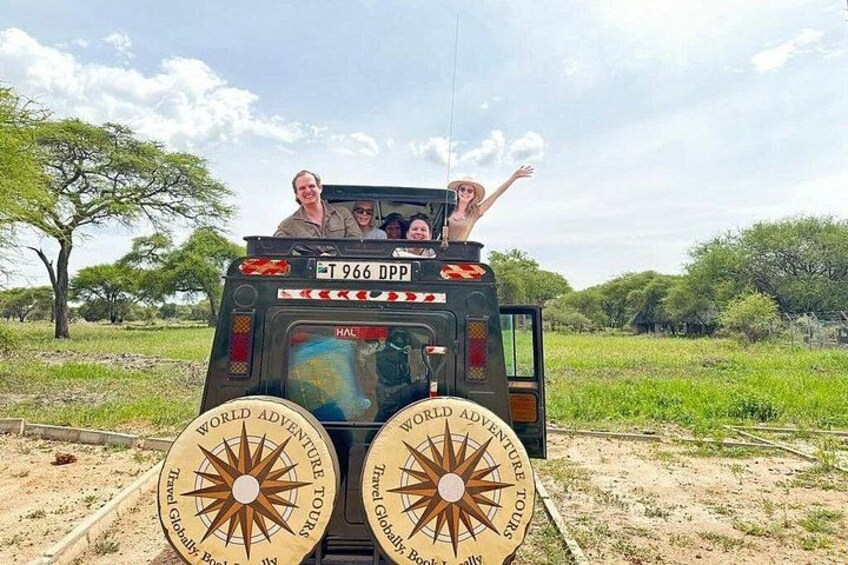 A safari vehicle with a sun emblem and the text 'WORLD ADVENTURES TOURS' on the back. 1