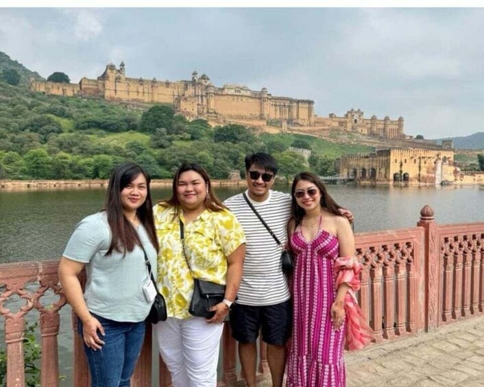A group of people standing by a river with a historic fort in the background. 1