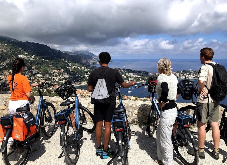 Four people on a coastal overlook with bicycles, overlooking a town and the sea. 1
