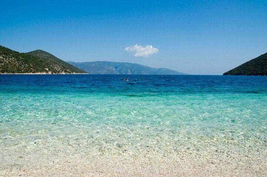 A clear turquoise sea, a sandy beach, and a hilly landscape in the distance. 3
