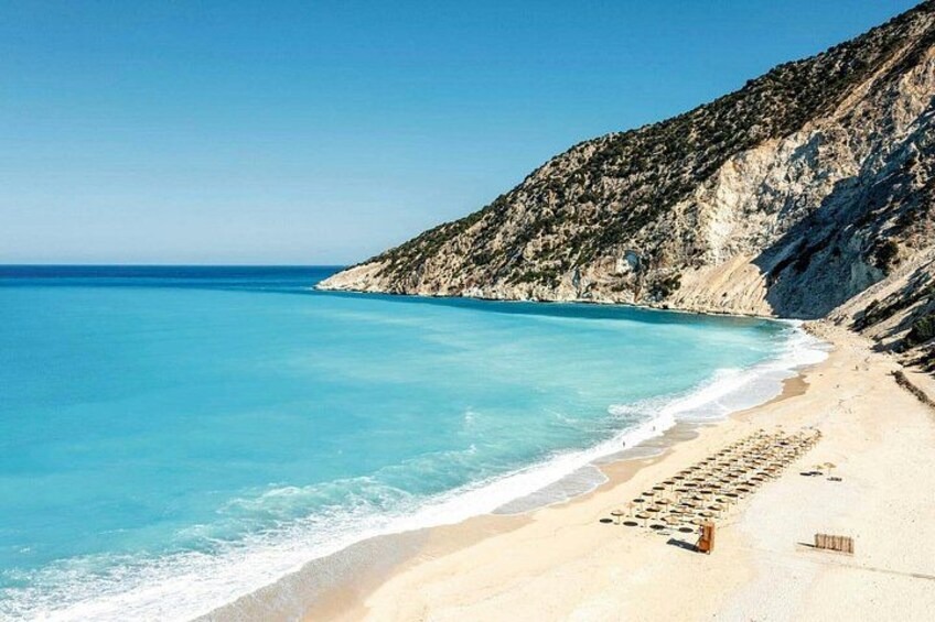 Una playa con agua turquesa cristalina, orilla arenosa y acantilados rocosos. 4
