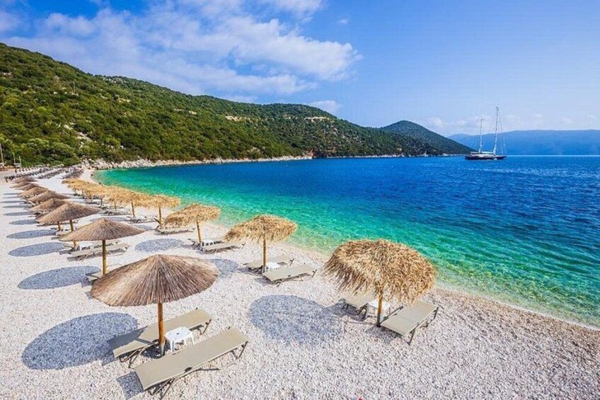 Una playa con sombrillas y sillas reclinables, un bote en el agua y un paisaje montañoso al fondo. 1