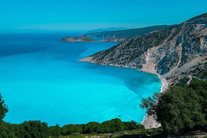 Un paisaje costero con aguas turquesas cristalinas, una playa arenosa y montañas al fondo. 5