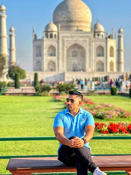 A man sitting on a bench with the Taj Mahal in the background. 5
