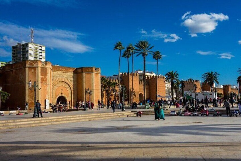 A historic gate with palm trees, a clear sky, and people in the square. 1
