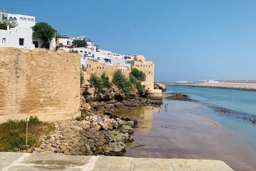 A coastal town with white buildings, a stone wall, and a beach. 3