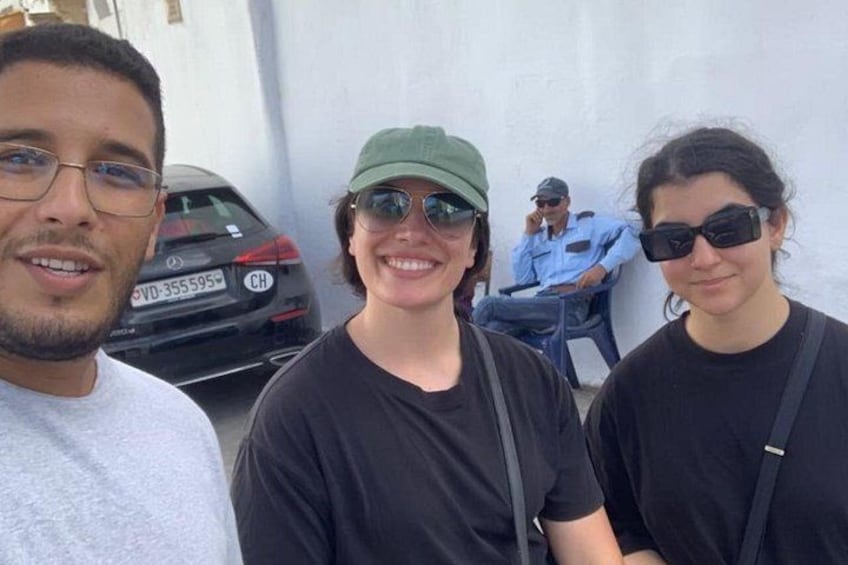 Three people standing in front of a building with a car in the background. 2