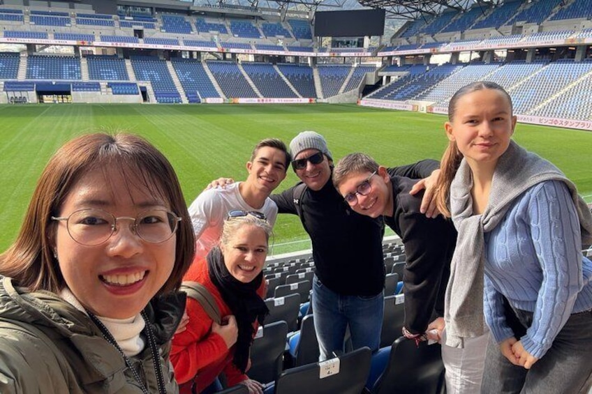 Un grupo de personas en un estadio con asientos azules vacíos y un campo verde. 1