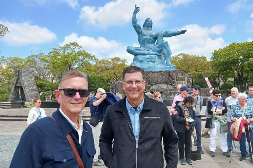 Two men standing in front of a statue with a blue sky and trees in the background. 3