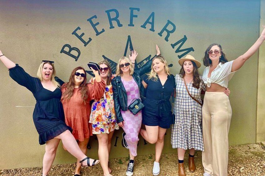 A group of people posing in front of a wall with 'BEER FARM' written on it. 4