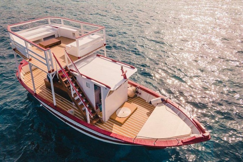 A red and white boat with a wooden deck, a covered seating area, and a staircase leading to an upper deck. 1