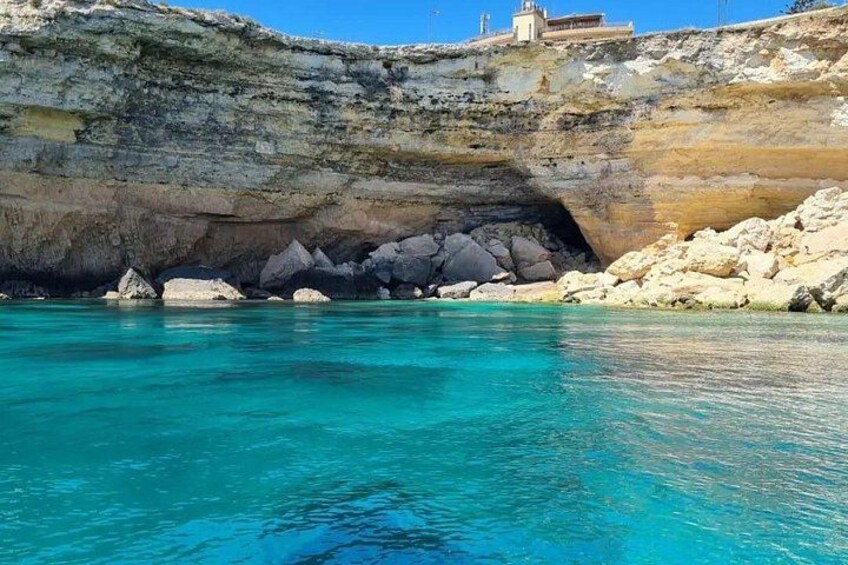 A coastal landscape with clear turquoise waters, rocky cliffs, and a small building on the cliff edge. 2