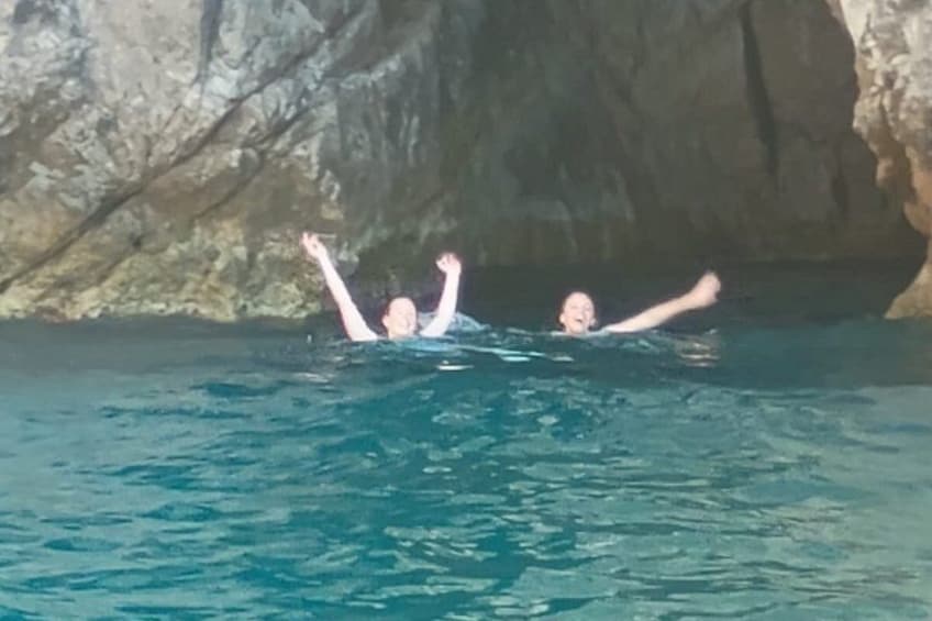 Two people swimming in a body of water with a rocky background. 5
