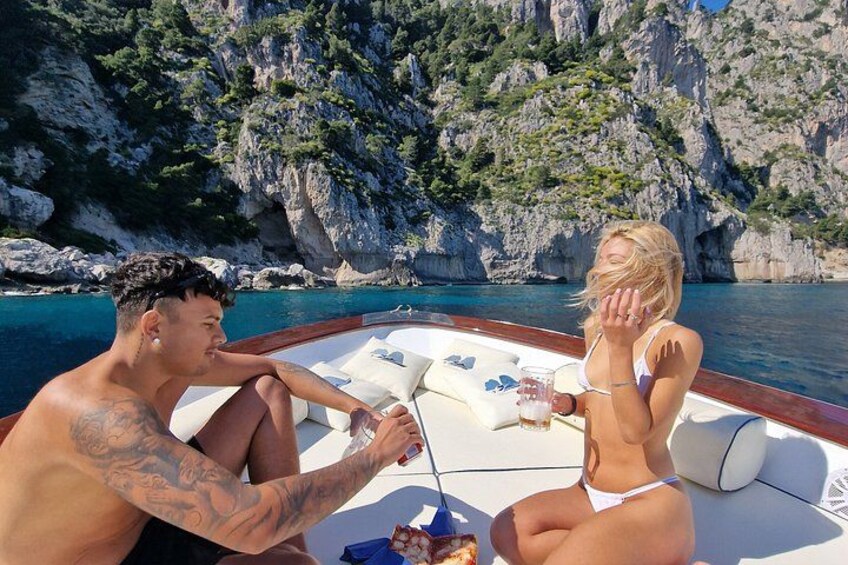 A boat with two people, rocky cliffs, and clear blue water. 2