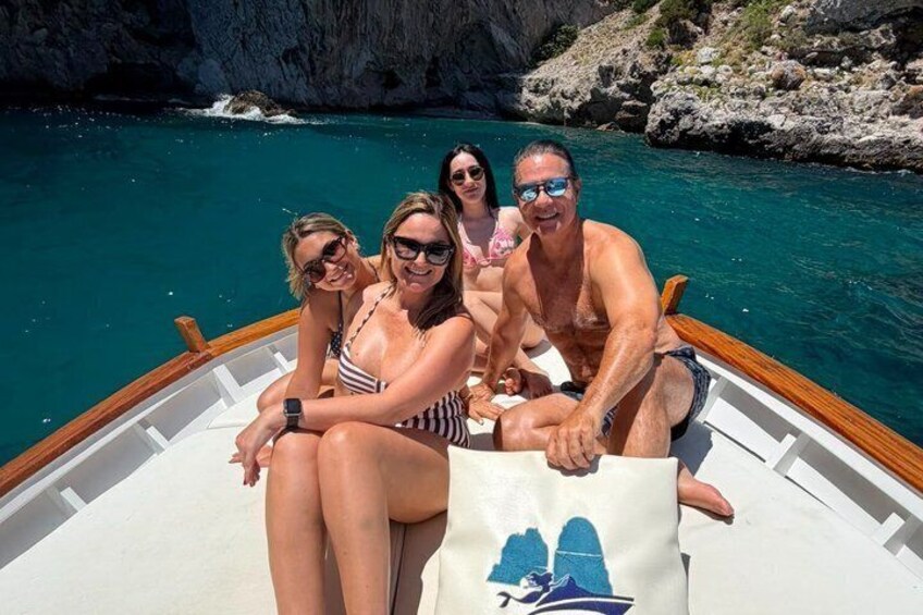 Un bote con gente en un mar azul cristalino, con acantilados rocosos al fondo. 4