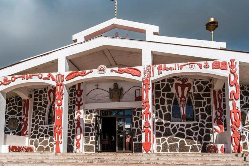 A building with a white facade and red decorative patterns, featuring a stone wall and a bell on top. 1
