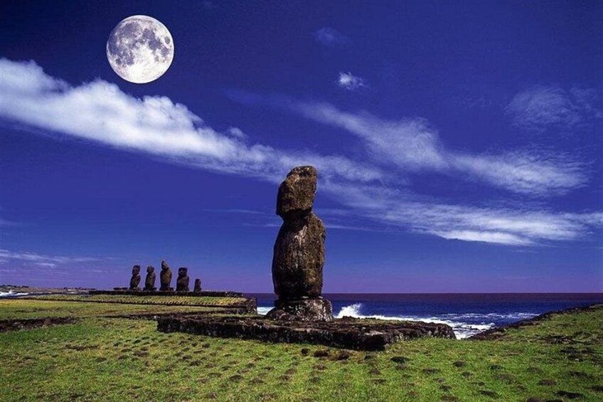 A large stone statue in a grassy field with a moon in the sky and a row of similar statues in the background. 5