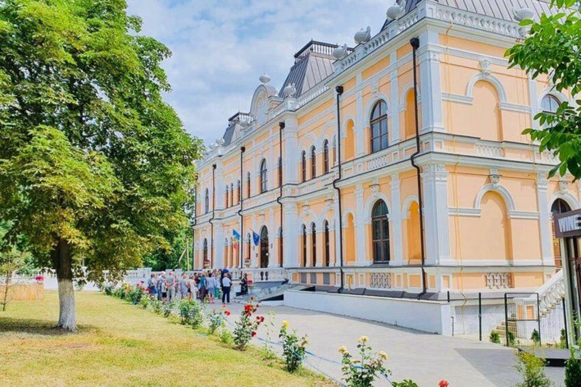 A historic building with classical architecture, a crowd of people, and a tree-lined pathway. 5