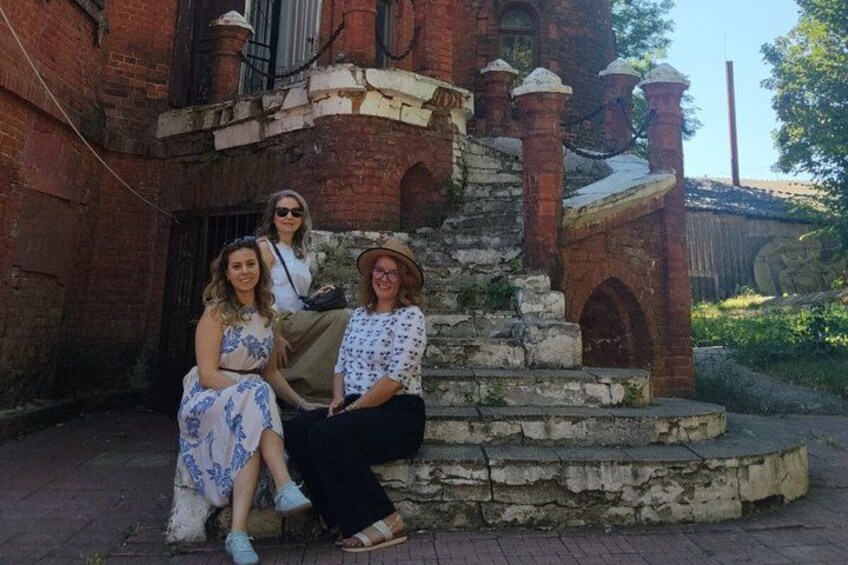 A group of people sitting on a stone staircase in front of a brick building with arched windows and a metal railing. 2