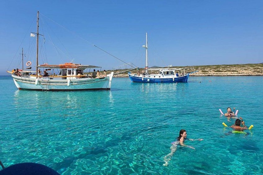 A clear blue sea with two boats, one anchored and one sailing, and a person swimming. 5